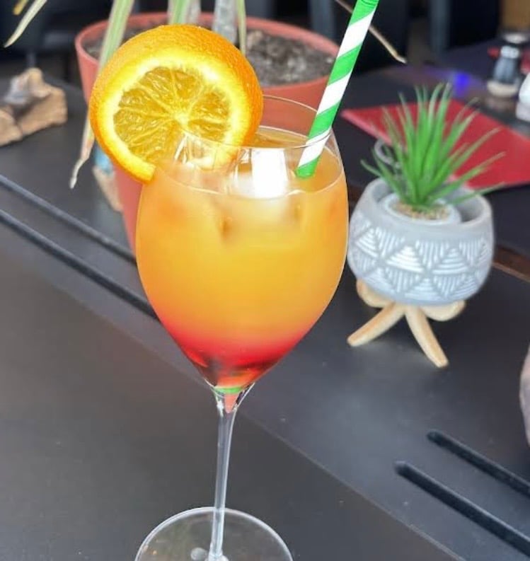 Tropical cocktail with orange slice garnish and green striped straw on dark bar counter