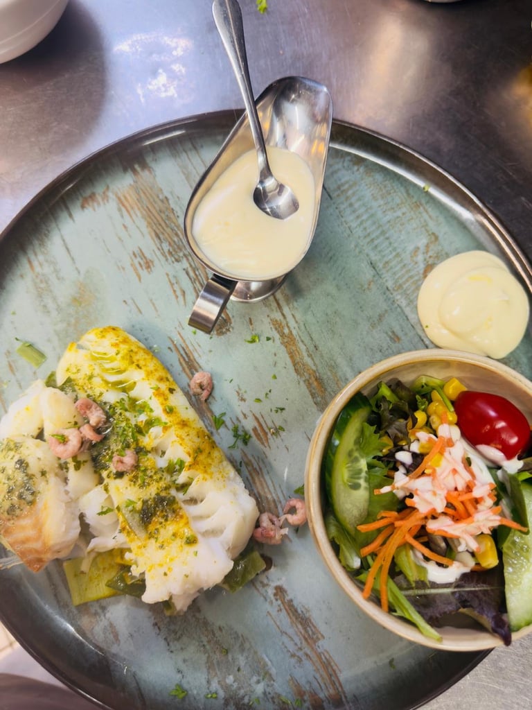Plated fish with herb topping, fresh vegetable salad, and sauce on a distressed blue-green plate with spoon