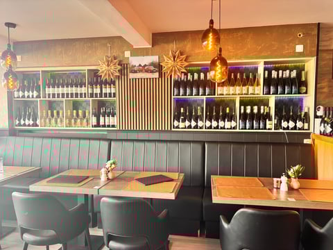 Modern wine bar interior with wooden tables, black chairs, and backlit wine bottle displays on shelves