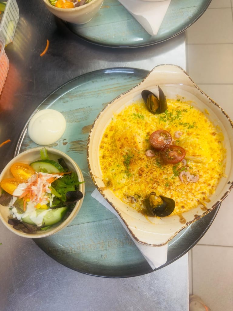 Overhead view of paella dish with yellow rice, mussels, clams, and meatballs, served with cucumber salad and white sauce on rustic blue plates