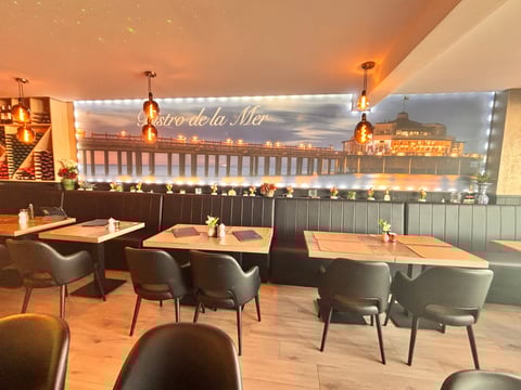 Upscale restaurant dining area with wooden tables, black chairs, and illuminated mural of seaside pier at night
