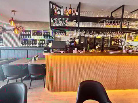 Modern restaurant or bar interior with orange countertop, shelving stocked with bottles, dark seating, and pendant lighting