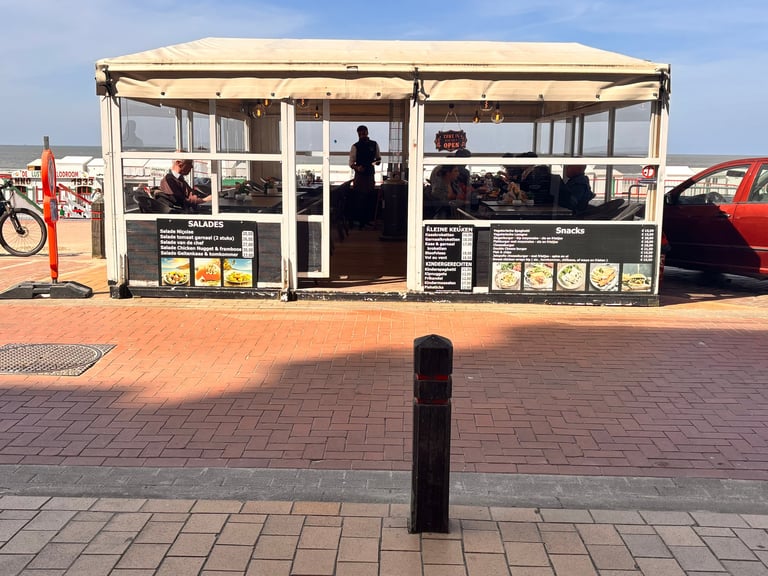Small vendor kiosk with beige canopy on a brick boardwalk, ocean and beach visible in background