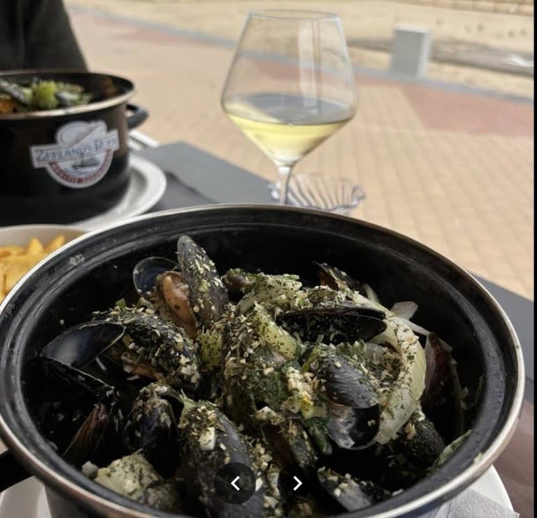 Bowl of mussels with herb sauce paired with white wine on an outdoor dining table