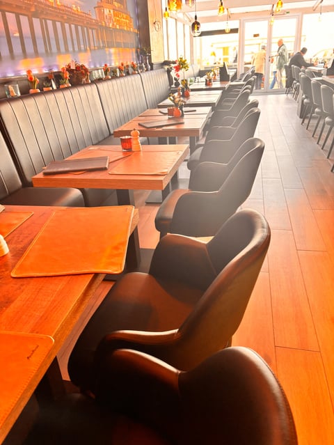 Modern restaurant interior with orange tables, black leather chairs, and booth seating lined along a corridor with hanging lights